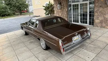 the back three quarters view of a brown 1979 Cadillac Coupe DeVille parked in front of the entrance to a building